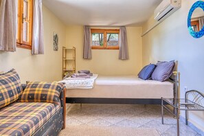A room with a bed, a sofa, a window, and an air conditioning unit.