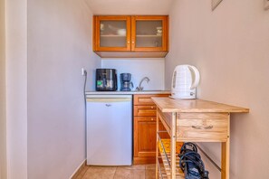 A compact kitchenette with a refrigerator, coffee maker, kettle, and a wooden table.