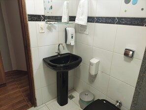 Un baño con lavamanos negro, dispensador de jabón, bote de basura y retrete.
