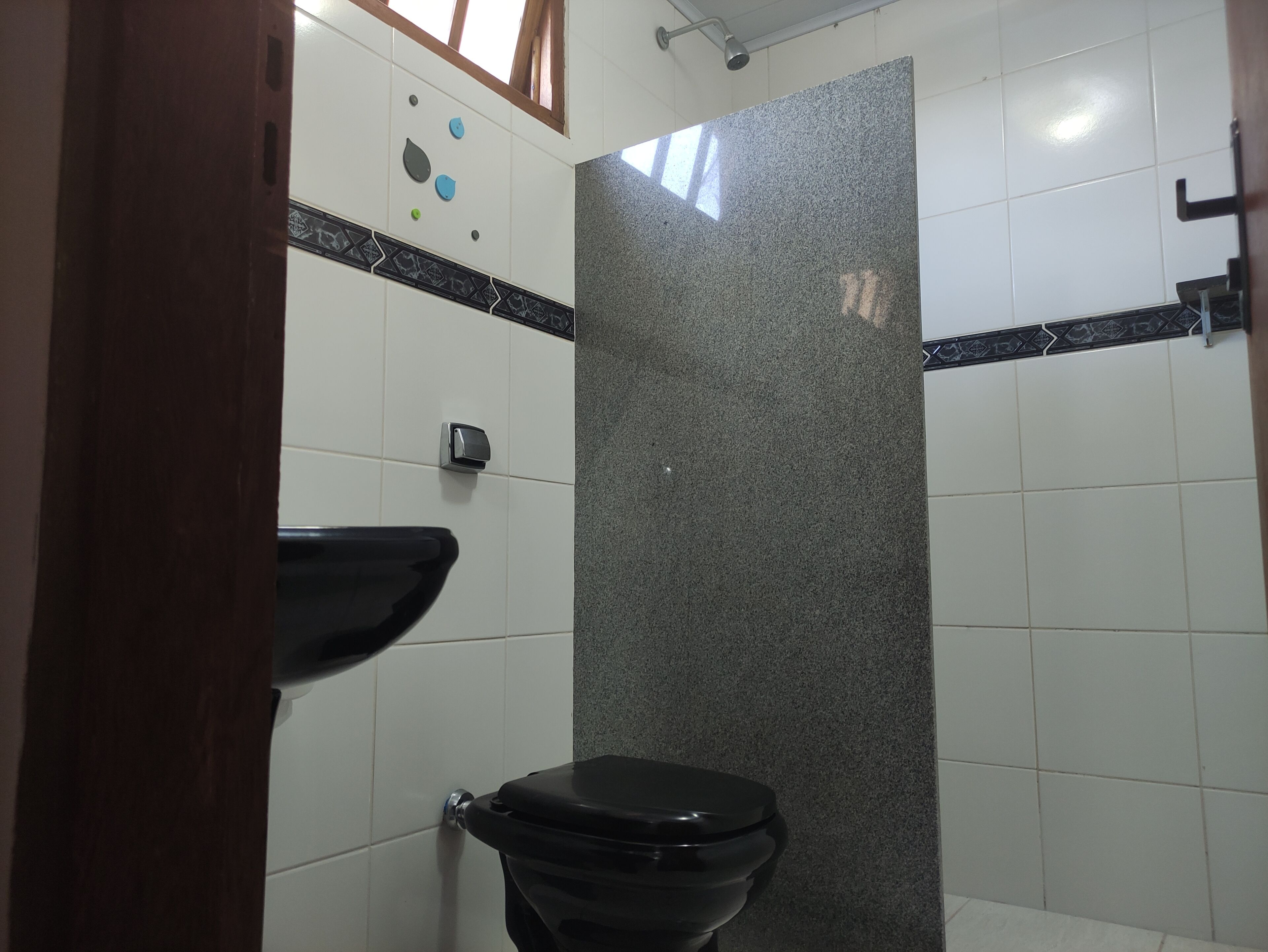 Un baño con inodoro negro, lavamanos y zona de ducha.