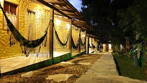A row of rooms with a stone pathway leading to a covered area, each room featuring a hammock and a window. - Pousada Templários Ecovilla  (Pirenópolis)