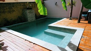 A swimming pool with a wooden deck and stone tiles, surrounded by plants and a stone wall. - Pousada Templários Ecovilla  (Pirenópolis)