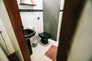 Casa de banho com sanita, lavatório e um contentor de lixo.
