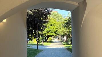 An arched corridor with a paved path leading to a park area with trees and a clear sky.
