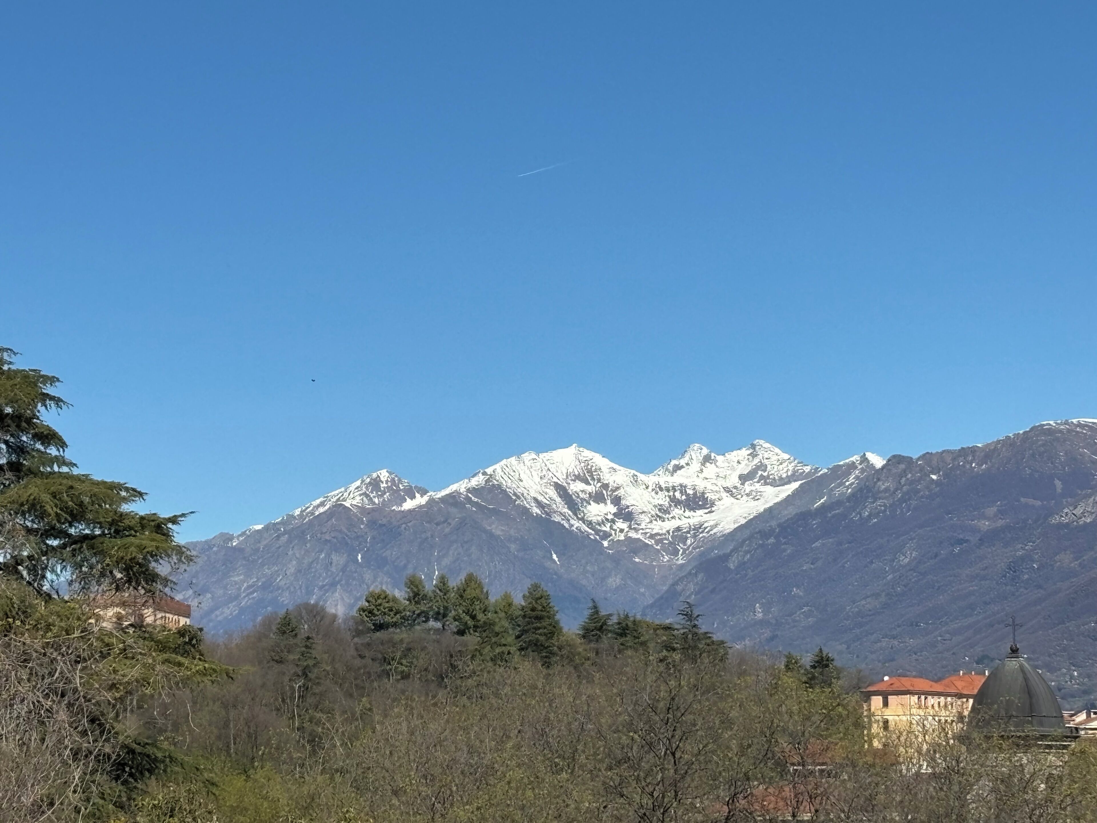Un paisaje montañoso con picos nevados, cielo despejado y un edificio con techo abovedado en primer plano.