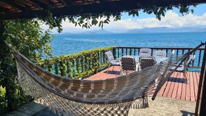 A hammock under a pergola, a table with chairs, and a view of the sea.