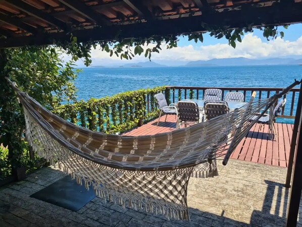 A hammock under a pergola, a table with chairs, and a view of the sea.