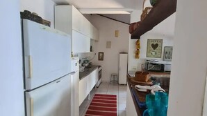 A narrow kitchen with white cabinets, a refrigerator, a red rug, and a coffee-themed wall decoration.