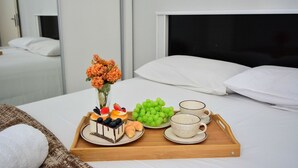 Una cama bien hecha con una bandeja de comida y bebidas, un jarrón de flores y una almohada blanca.