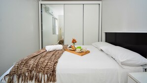 Habitación de hotel con cama, mesita de noche, bandeja de desayuno, espejo y armario.
