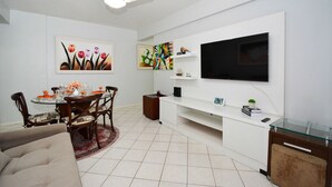 Una sala de estar con comedor, un televisor de pantalla plana montado en la pared y un ventilador de techo.