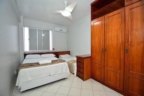 A bedroom with a bed, a nightstand, a wooden wardrobe, a ceiling fan, and a window.