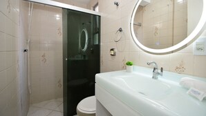 Un baño con cabina de ducha de vidrio, un inodoro, un lavabo con espejo y una toalla sobre el lavabo.