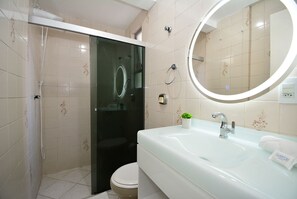 Een badkamer met een douchecabine van glas, een toilet, een wastafel met spiegel en een handdoek op de wastafel.
