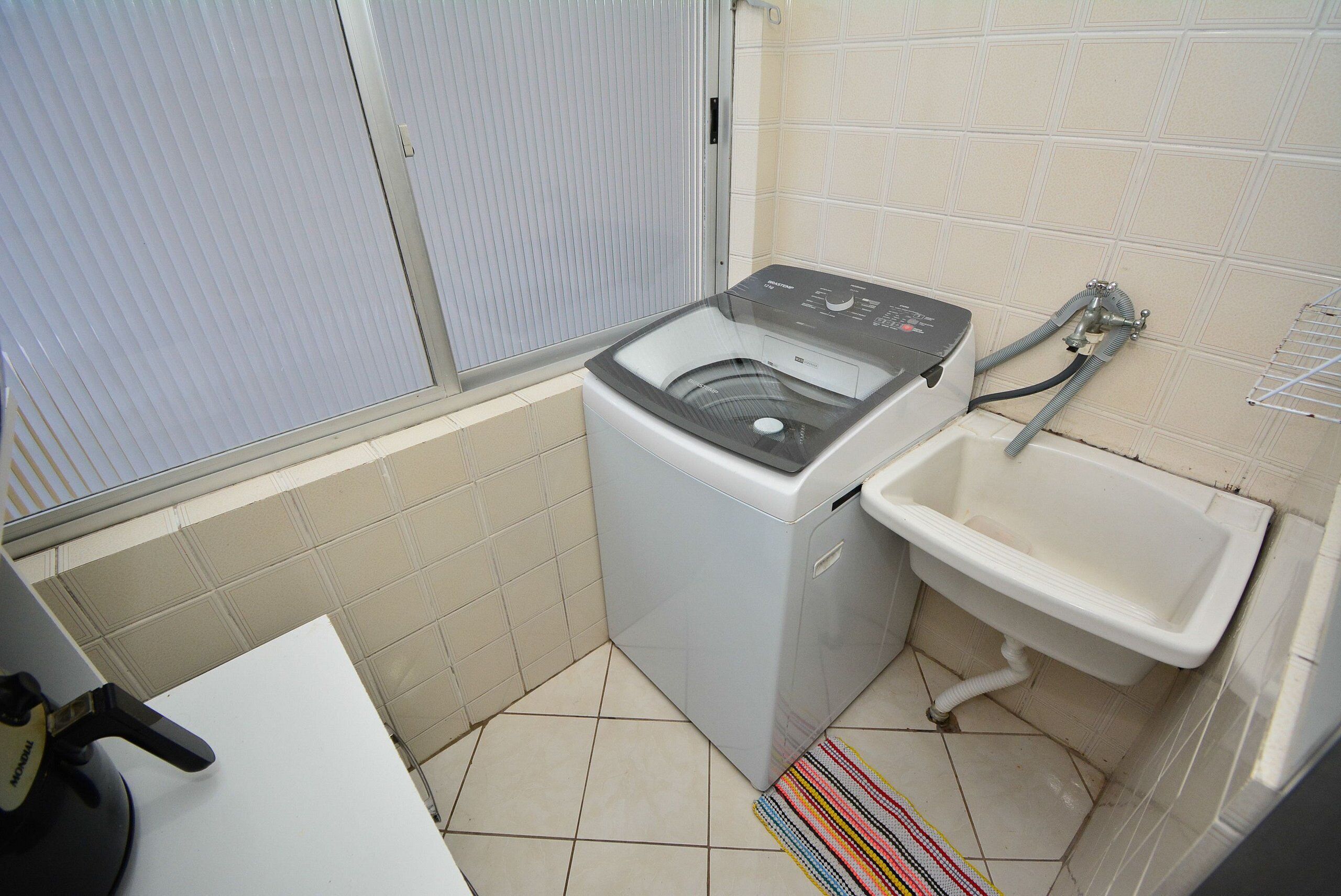 Een kleine wasruimte met een wasmachine, een wasbak en een betegelde vloer.
