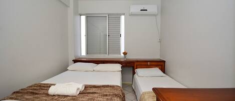 A bedroom with two beds, a window, a desk, and an air conditioning unit.