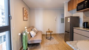 A compact living space with a sofa, a small round table, a refrigerator, and a microwave. - Barrio París Londres - Domus Travels (Santiago)