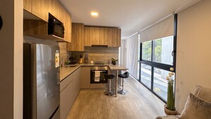 A modern kitchen with wooden cabinets, stainless steel appliances, and a large window offering a view of the street. - Barrio París Londres - Domus Travels (Santiago)