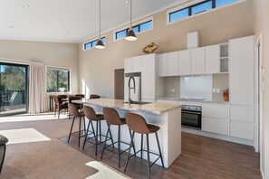 A modern kitchen with a central island, bar stools, and a dining area with a view. - Riverstone Retreat - Turangi Holiday Home (Turangi)