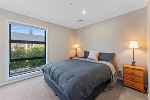 A bedroom with a large window, a bed, two bedside tables with lamps, and a nightstand. - Riverstone Retreat - Turangi Holiday Home (Turangi)