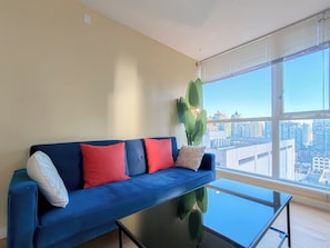 Una sala de estar moderna con un sofá azul, una mesa de centro de vidrio y un ventanal con vistas a la ciudad.