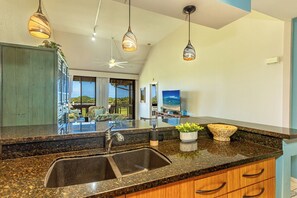 A kitchen with granite countertops, a double sink, pendant lighting, and a view of the outdoors. - GC 148-Front-Row Sunsets Over the Ocean and Golf Course | Wailea Luxury 2BR (Kihei)