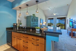 A modern kitchen with a large island, pendant lighting, and a view to the outdoors. - GC 148-Front-Row Sunsets Over the Ocean and Golf Course | Wailea Luxury 2BR (Kihei)