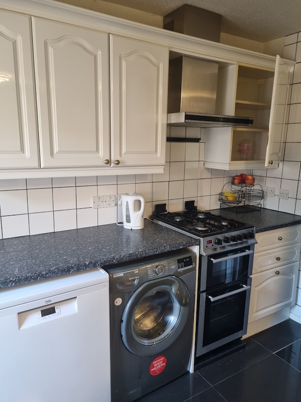 A compact kitchen with white cabinetry, a built-in oven, a washing machine, and a coffee maker.