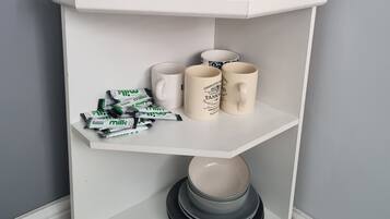 A corner shelf unit with a vase of flowers, a wooden decorative item, and a mug with text.