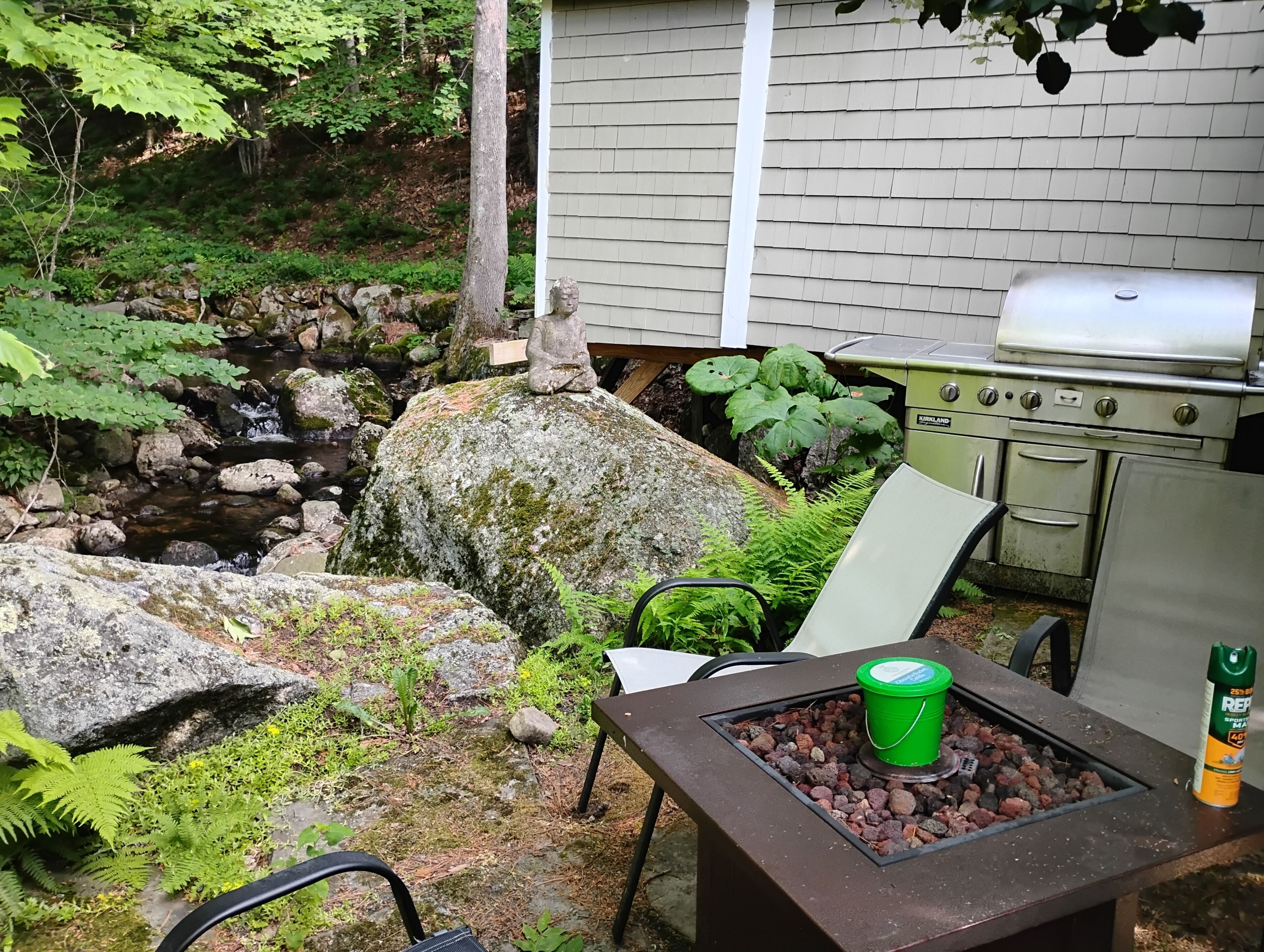 En trädgård med ett vattenfall av sten, en grill och ett bord med en hink.