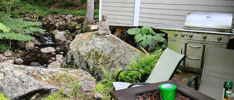 A backyard with a stone waterfall, a grill, and a table with a bucket.
