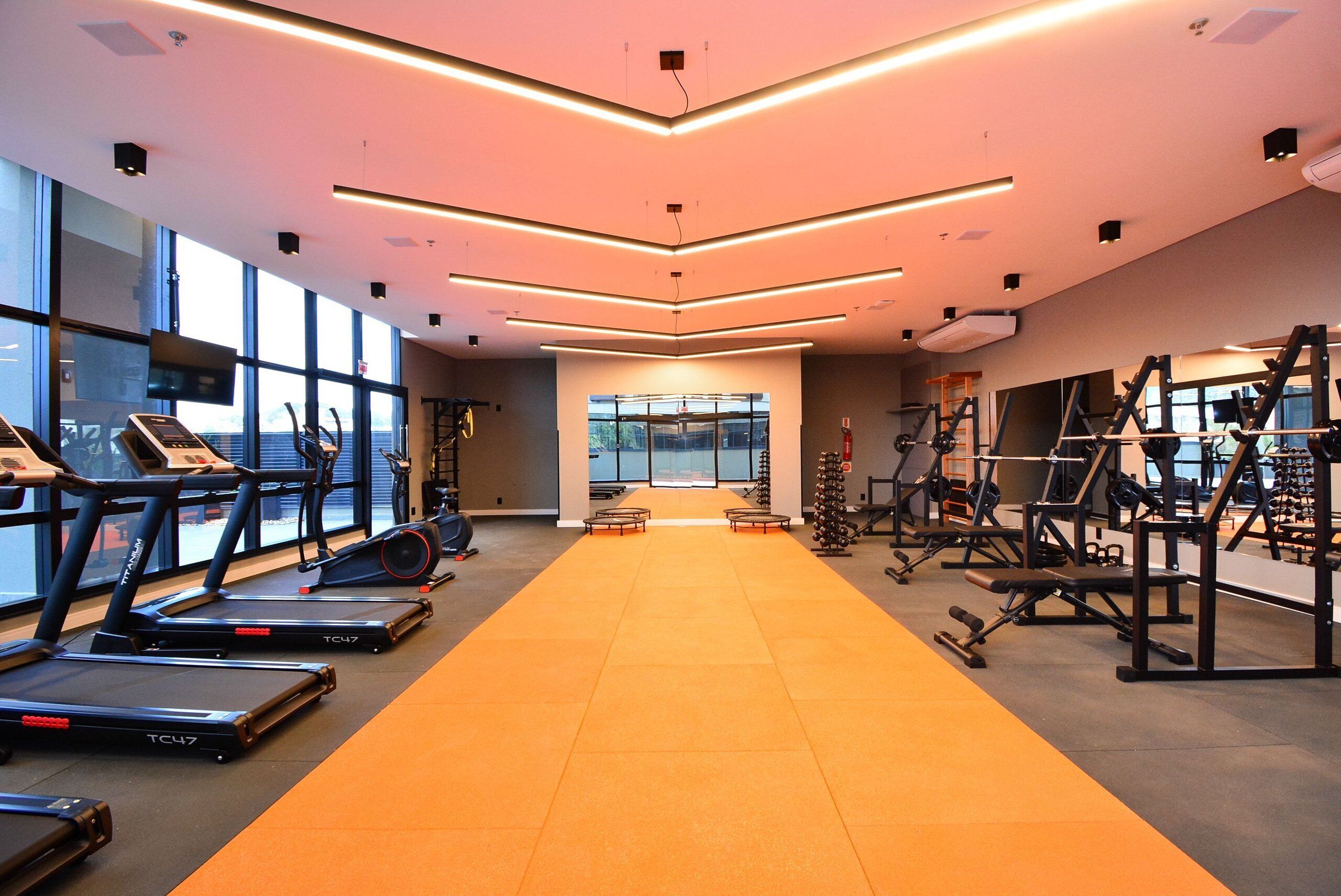 A modern gym with treadmills, weight machines, and a central orange mat.