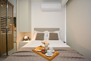 Una cama bien hecha con una bandeja de desayuno, una lámpara de noche y un equipo de aire acondicionado arriba.