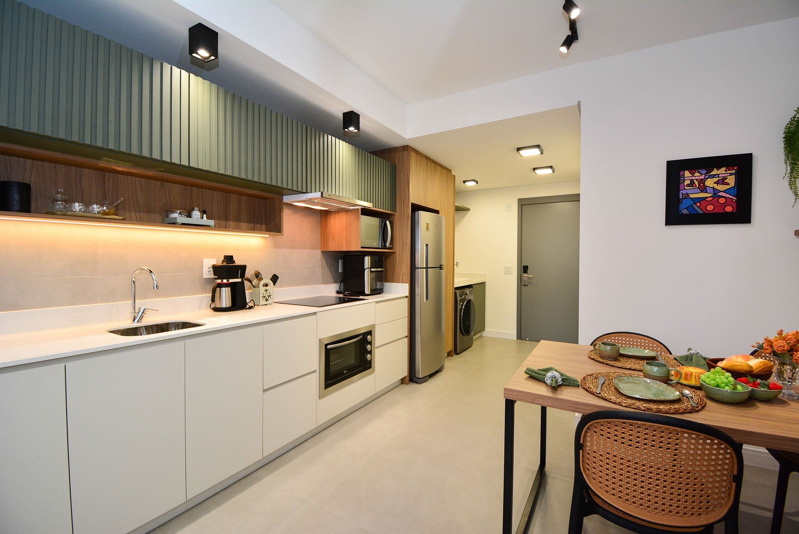 Una cocina moderna con electrodomésticos integrados, una zona de comedor con mesa y sillas, y una pequeña mesa de comedor dispuesta con platos y cubiertos.