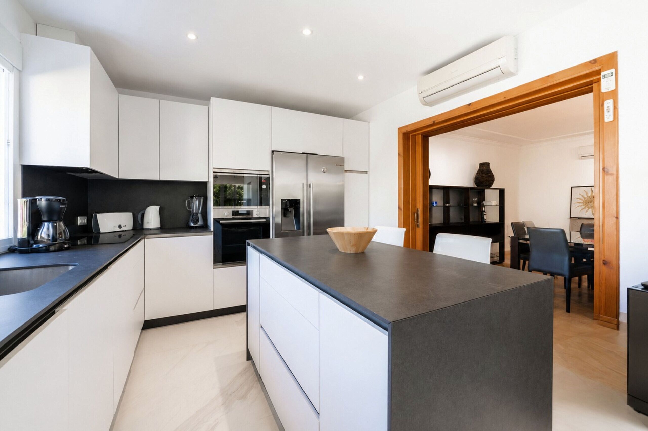 Une cuisine moderne avec des meubles blancs, un îlot central, un four encastré et un réfrigérateur.