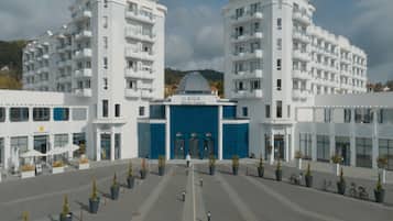 A modern hotel with a central blue facade, multiple balconies, and a surrounding courtyard with potted plants.