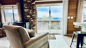 A cozy room with a stone fireplace, a sofa, a dining table, and a view of the outdoors. - Forest Ridge Cabin - Pet Friendly - Sleeps 10 (Ahwahnee)