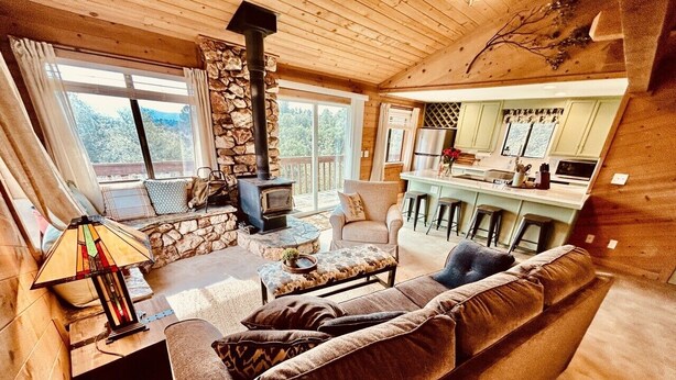 A cozy cabin interior with a stone fireplace, a sofa, a dining area, and a kitchen. - Forest Ridge Cabin - Pet Friendly - Sleeps 10 (Ahwahnee)