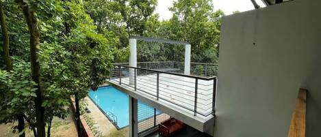 A modern building with a balcony overlooking a swimming pool, surrounded by trees.
