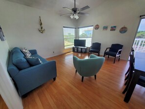 Ein Wohnzimmer mit einem blauen Sofa, einem türkisfarbenen Sessel und einem Fernseher auf einem Lowboard.