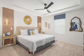 Ein Schlafzimmer mit einem Bett, Nachttischen, einem Deckenventilator, Wandleuchten, einem Zier-Spiegel und einer Uhr.