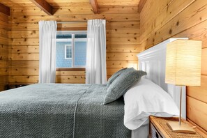En stuga med träpanel, inredd med en säng, gardiner, ett fönster och en sänglampa.