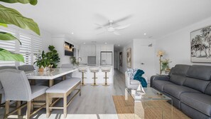 A modern living room with a grey sofa, a dining area with a white table and grey chairs, and a kitchen with white cabinets and a white ceiling fan. - luxurious 2 bedroom unit on Maroochydore River (Maroochydore)