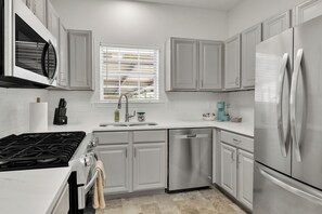 Una cocina moderna con armarios blancos, electrodomésticos de acero inoxidable, lavavajillas y una ventana con persianas.