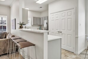 Una cocina moderna con armarios blancos, un refrigerador de acero inoxidable y una zona de bar con taburetes.