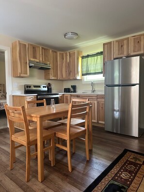 Una cocina con armarios de madera, un refrigerador de acero inoxidable, una estufa y una mesa de comedor con sillas.
