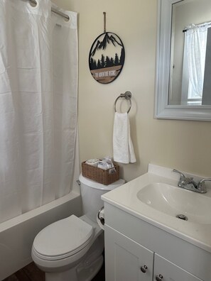 Un baño con inodoro, lavamanos, espejo, toallero y cortina de ducha.