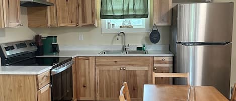 A kitchen with wooden cabinets, a stainless steel refrigerator, a stove, and a dining table with chairs.