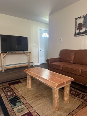 Una sala de estar con un televisor sobre un soporte de madera, un sofá de cuero marrón y un banco de madera.
