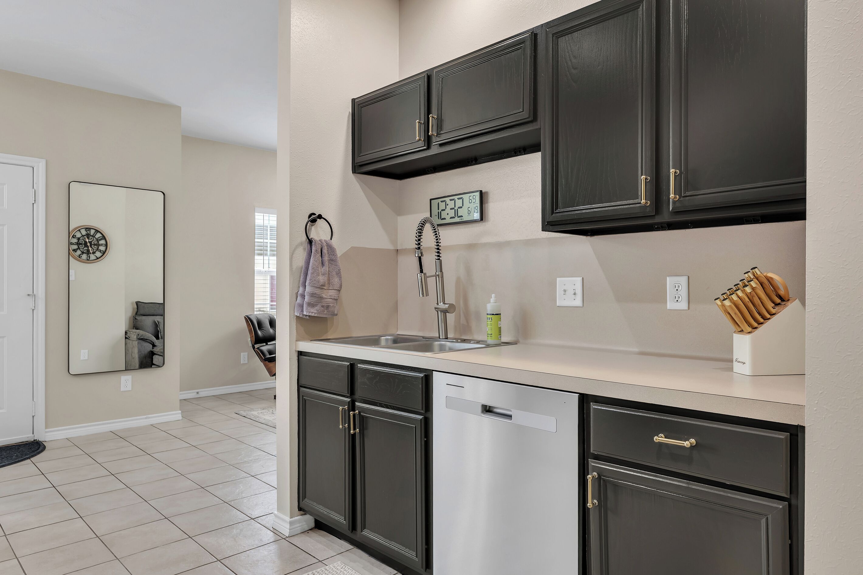 A kitchen with dark cabinets, a stainless steel dishwasher, a clock, and a knife block.